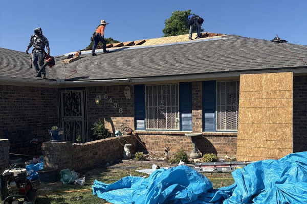 Two roofers tearing off old shingles on a brick home with tarps protecting the landscaping in Haslet, TX