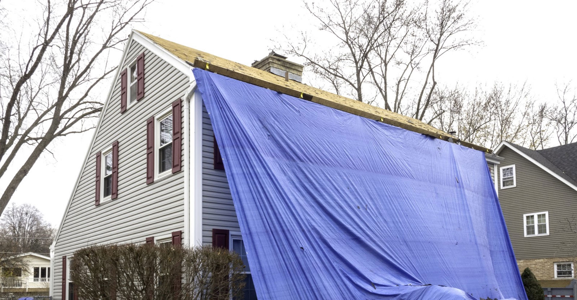 Home with a blue emergency tarp draped over a storm-damaged roof slope in Haslet, TX