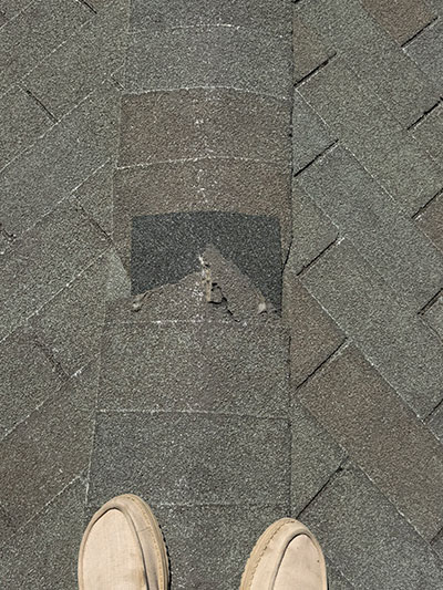 Roofer standing over a patched section of shingles, boots in frame in Haslet, TX